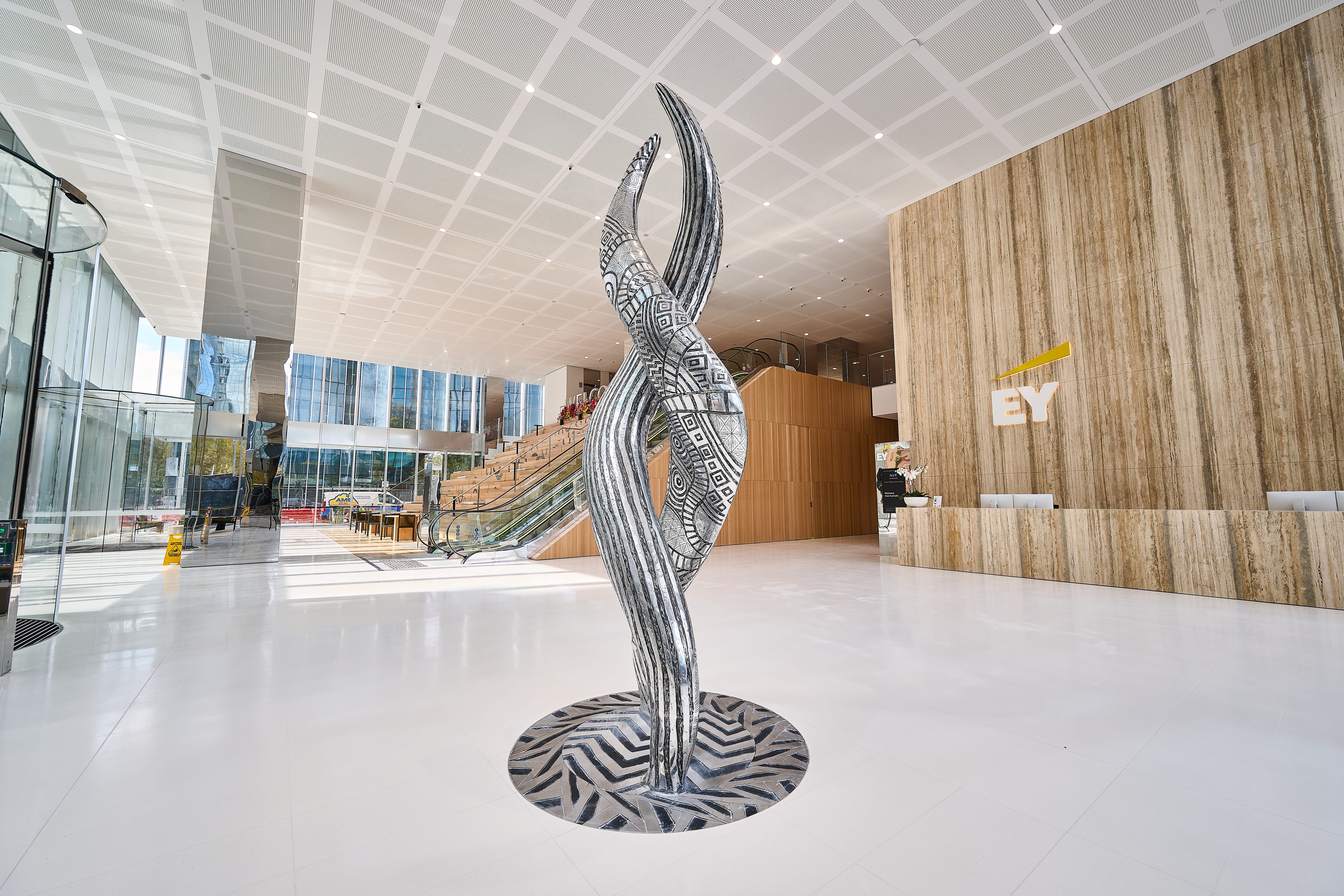 9 by Brett Nannup, a vertical sculpture, two pieces entwined sitting on a white floor in the middle of a large reception area