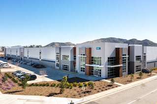 A white building with brick columns and some landscaping around the parking lot