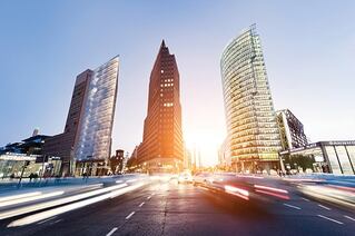 View of three skyscrapers, taken at street level. Cars are rushing by on both sides.