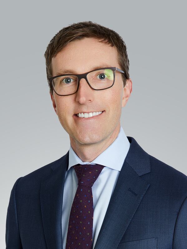 Headshot of a man in a blue suit and light colored shirt wearing a tie and glasses.