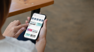 A woman holding mobile phone and looking at the programs offered through the axiis tenant app.