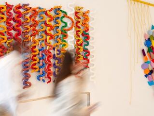 Colorful pieces of artwork along a wall in a lobby and two individuals walking past it up a set of stairs