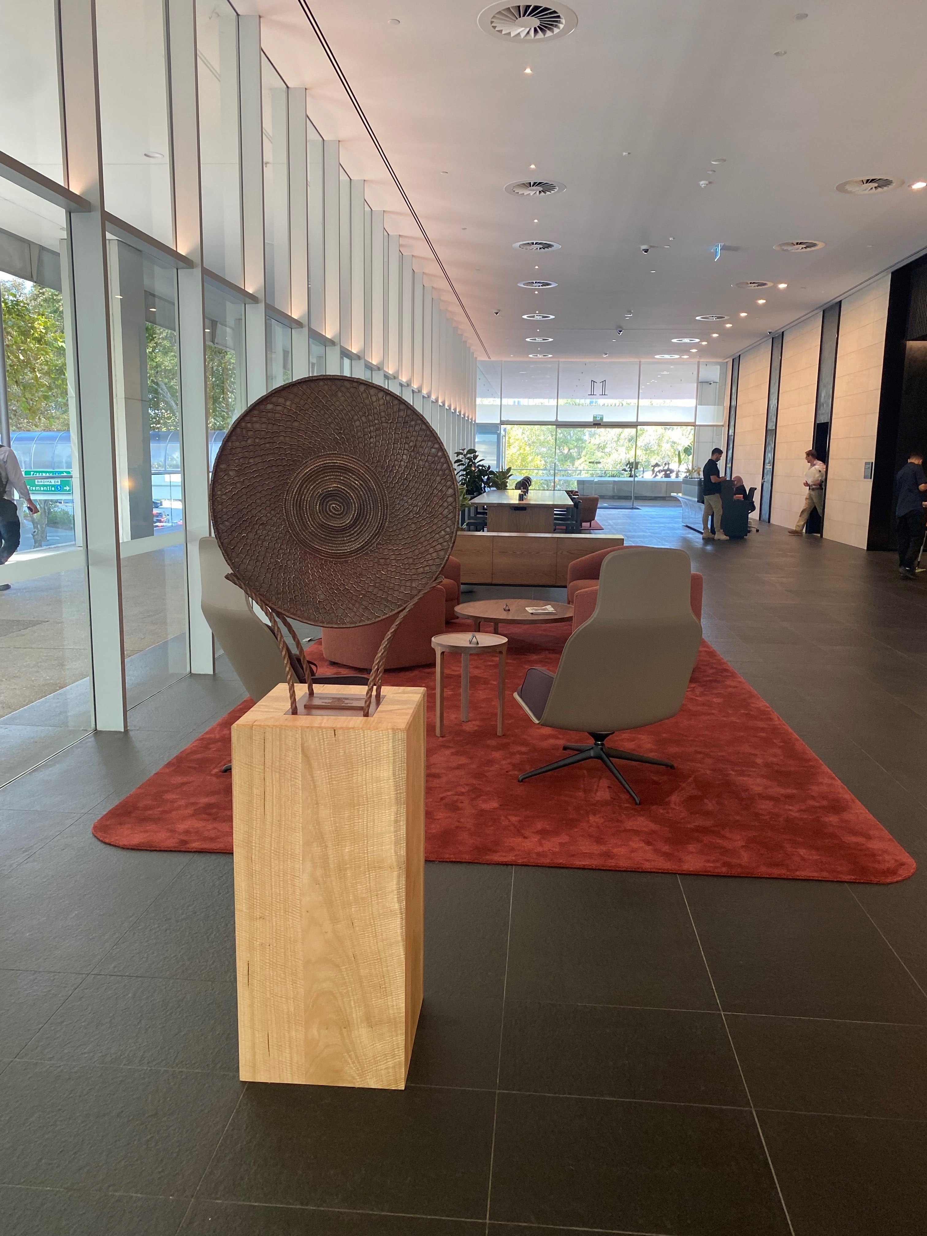 Gabbi Didup Yeb, created by Lea Taylor, sculpture in the middle of a room, glass windows the the left of the sculpture and a red rug on the floor with seating