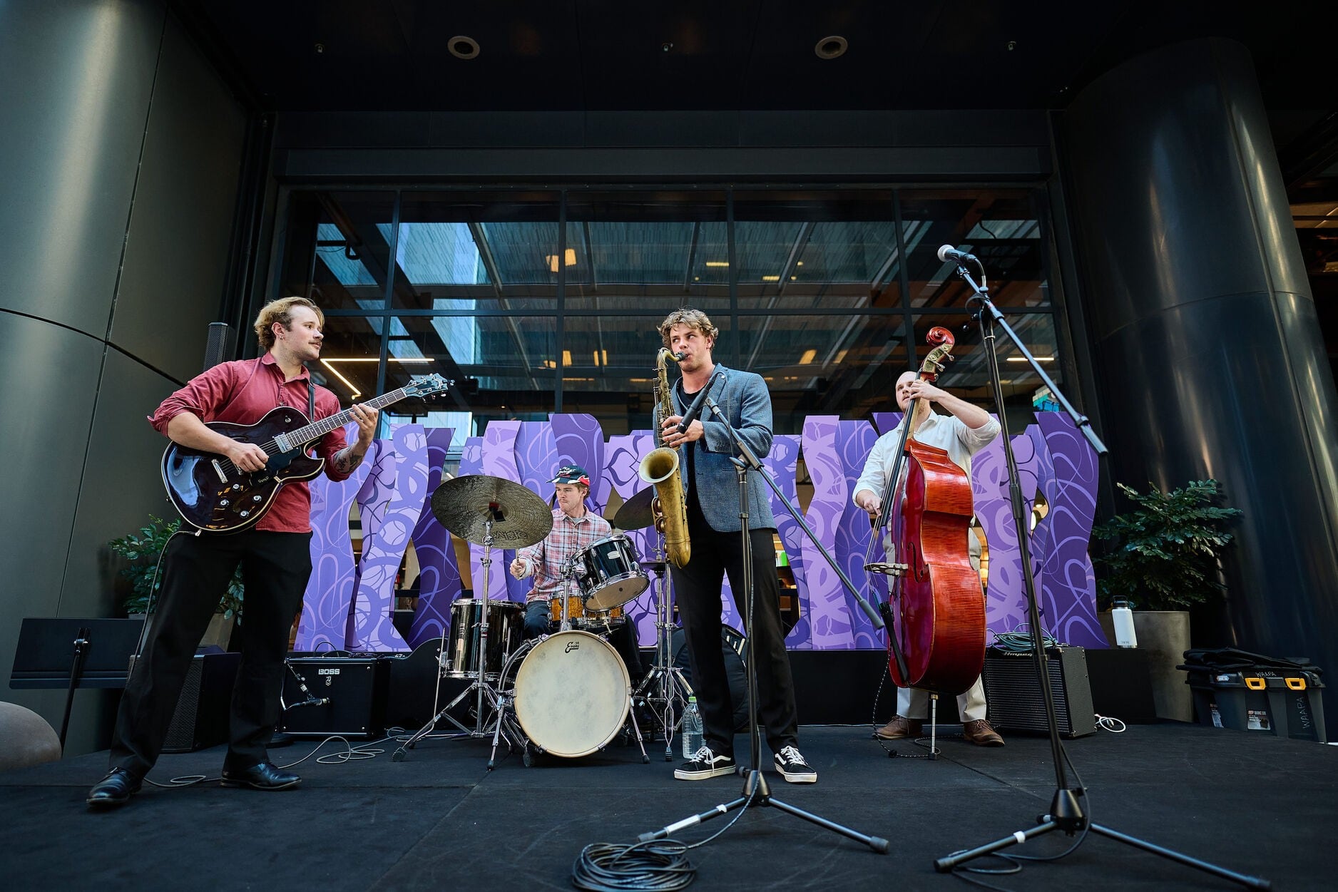 a music band playing the guitar, drumset, saxophone and bass cello on stage