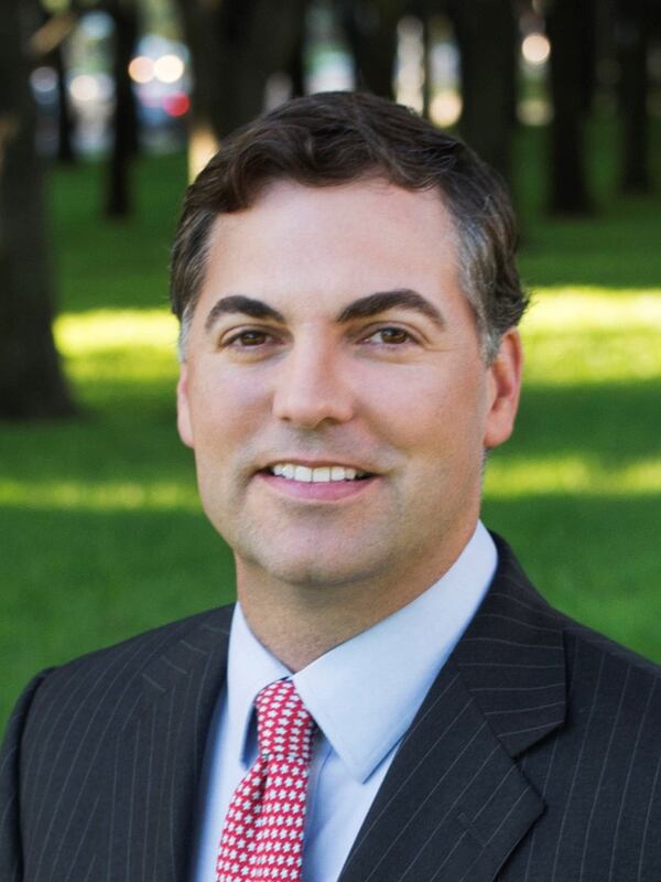 Photo of a man wearing a suit with a red tie with greenery and trees in the background