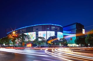 A building with a blue light along the top of it is situated near a bustling city road.