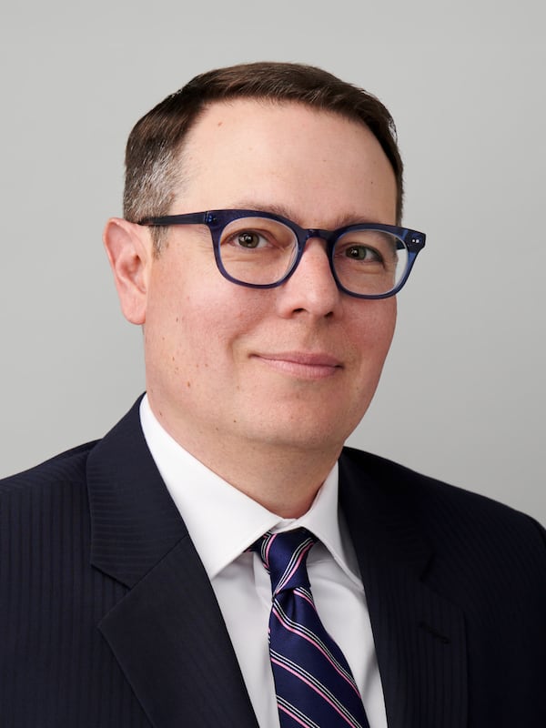 Headshot of a man wearing a suit and glasses, smiling for camera