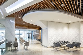 There is a modern looking room with a ceiling that has many slits along it. The walls are white and the ceiling is brown.