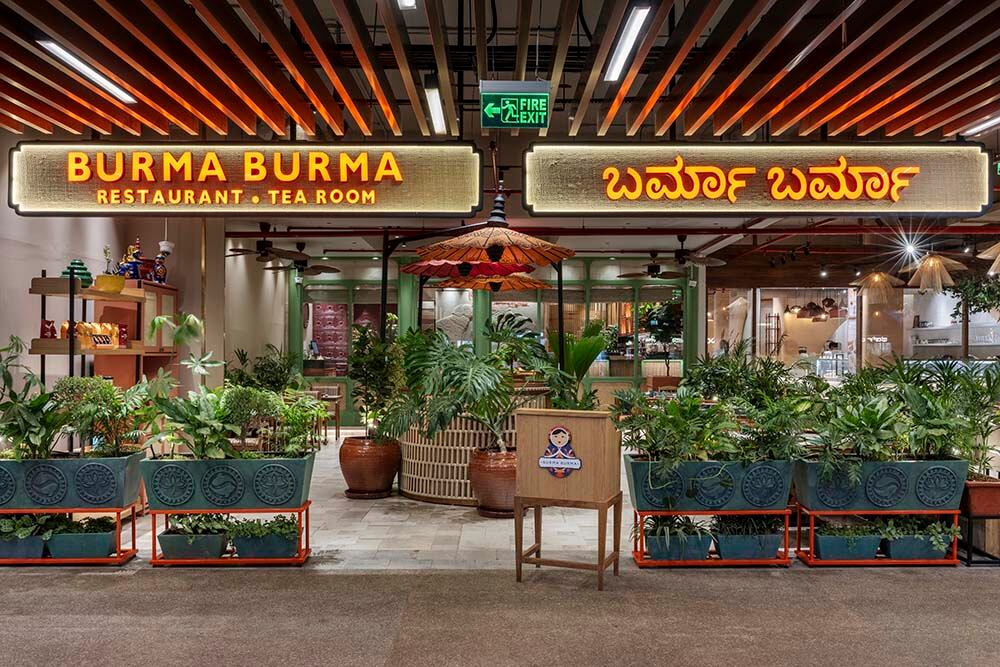Exterior of Burma Burma Restaurant & Tea Room with lush greenery and warm wooden signage.