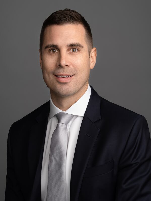 A male headshot,  with a friendly smile, dressed in a business suit, shirt and tie