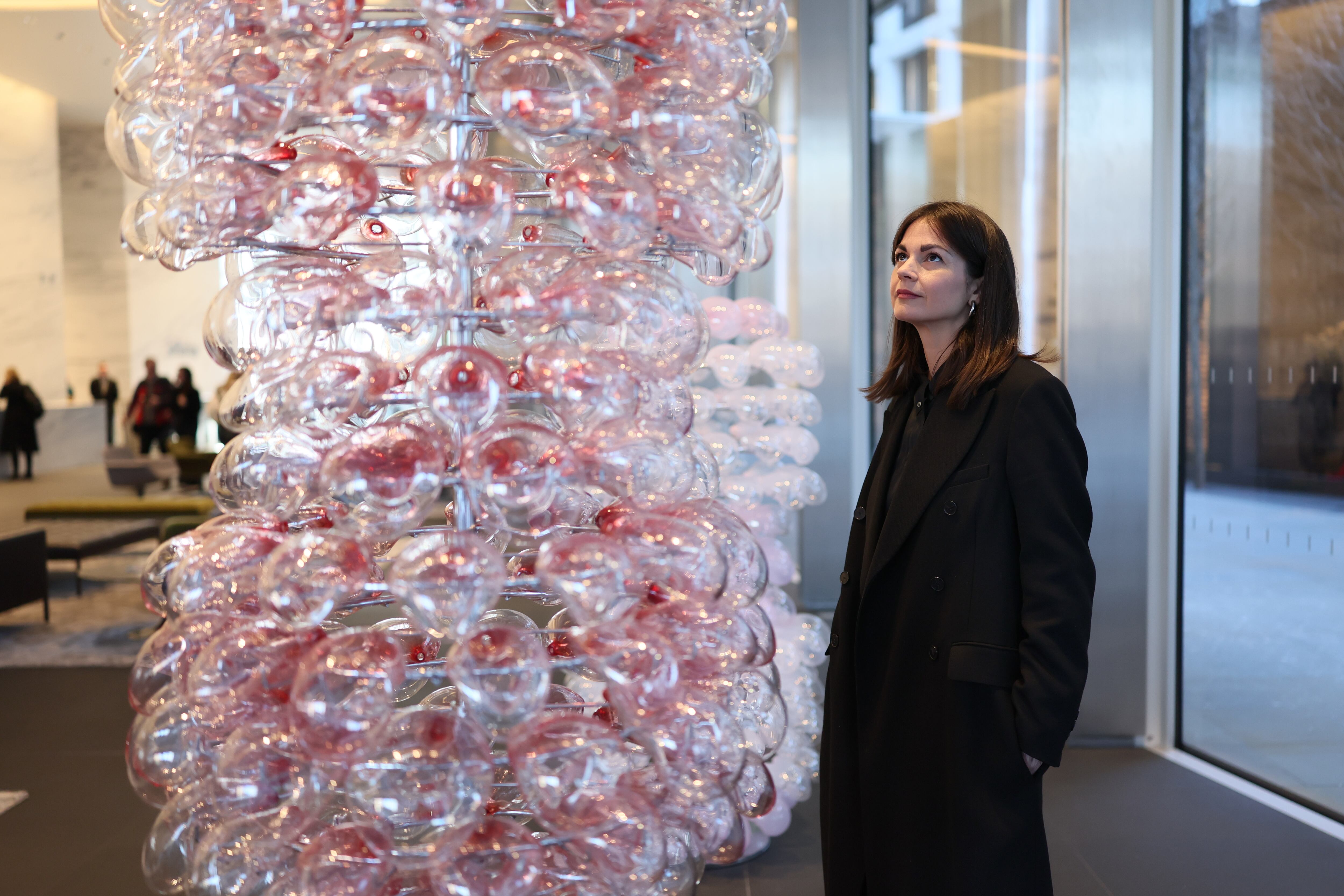 Women in black long outerwear standing looking up at a sculpture made of clear and red blown glass