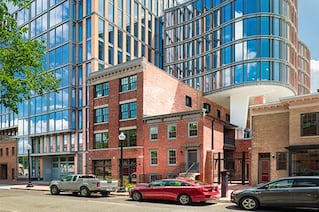 Street level view of a curved, glass building. Three cars are parked on the opposite side of the road.