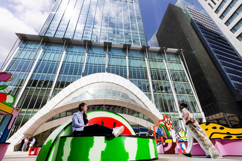 A colorful public art installation featuring bold, cartoon-like figures and vibrant floral designs. The artwork uses thick black outlines and bright, saturated colors.