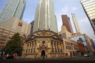 Many large skyscrapers tower over an older style building in the middle of a city.