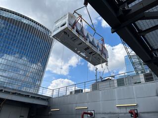 Utility equipment elevated by a crane towards the rooftop of an office building