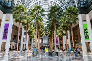 Trees that are in an indoor mall with people walking around on the tile flooring.