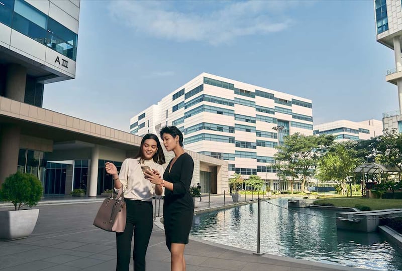 Two women looking at a cell phone in front of a reflecting pool that is located in front of an office building