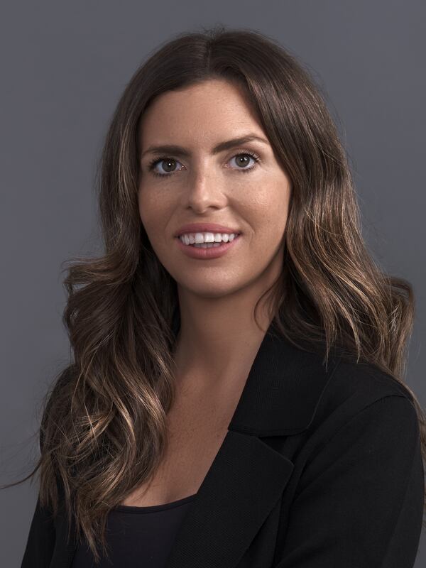 A female headshot, with a friendly smile, dressed in a business jacket and shirt