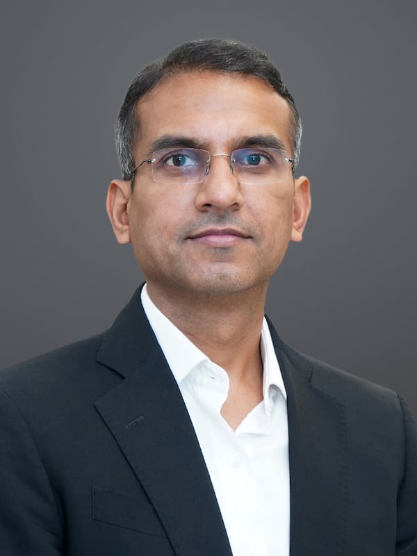 Headshot of a man wearing a white button down shirt and black blazer wearing glasses