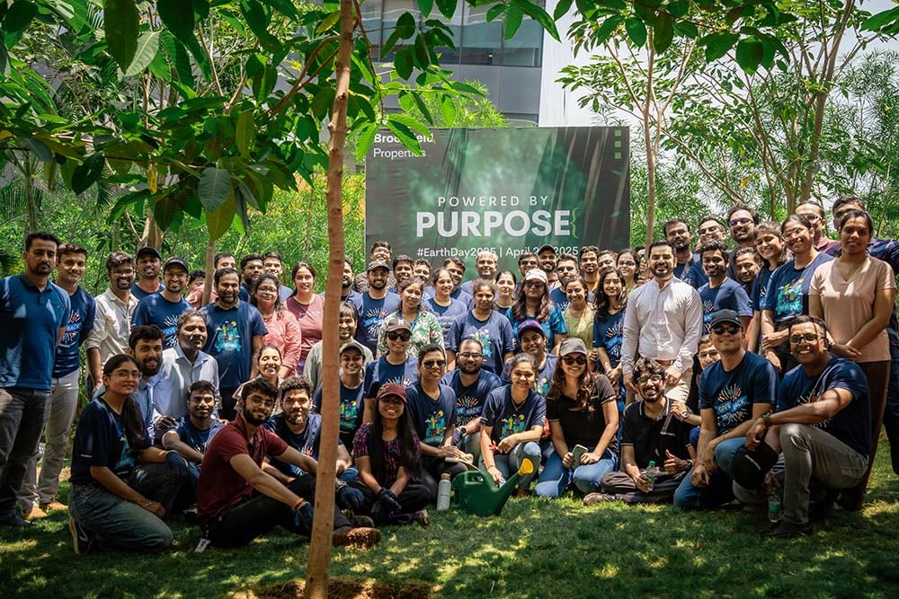 Large group of Brookfield Properties team members posing outdoors during a corporate event, standing in front of a 'Purpose' sign surrounded by greenery.