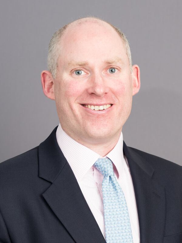 headshot of a white man in a suit with a blue blazer, a white shirt and a light blue tie