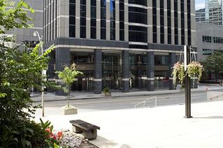 A tiled courtyard with some hanging plants and bushes at the side. Over the road is an imposing dark building.