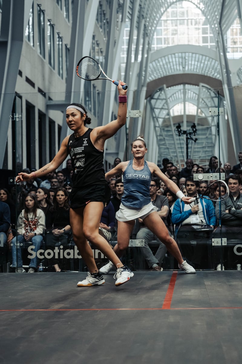 Two women playing squash with an audience