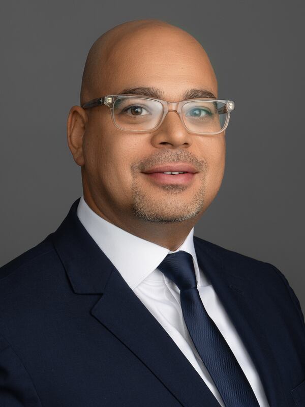 Male headshot, with a friendly smile, dressed in a business suit, shirt and tie