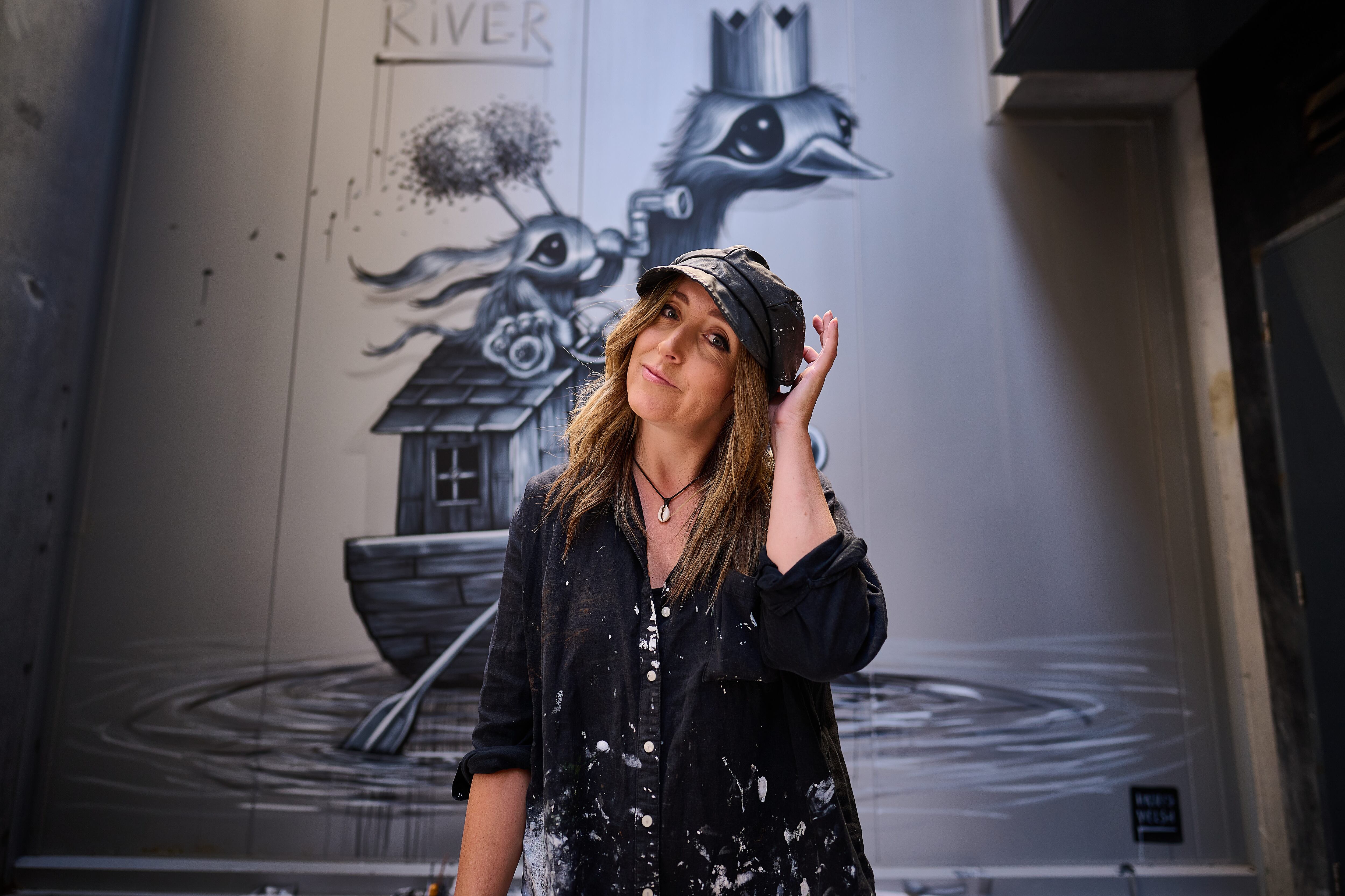 Street art mural depicting a whimsical black-and-white emu wearing a crown and carrying a mouse with a flower hat in a small boat.