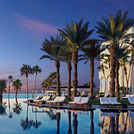 poolside at dusk with palm trees and hotel in the background