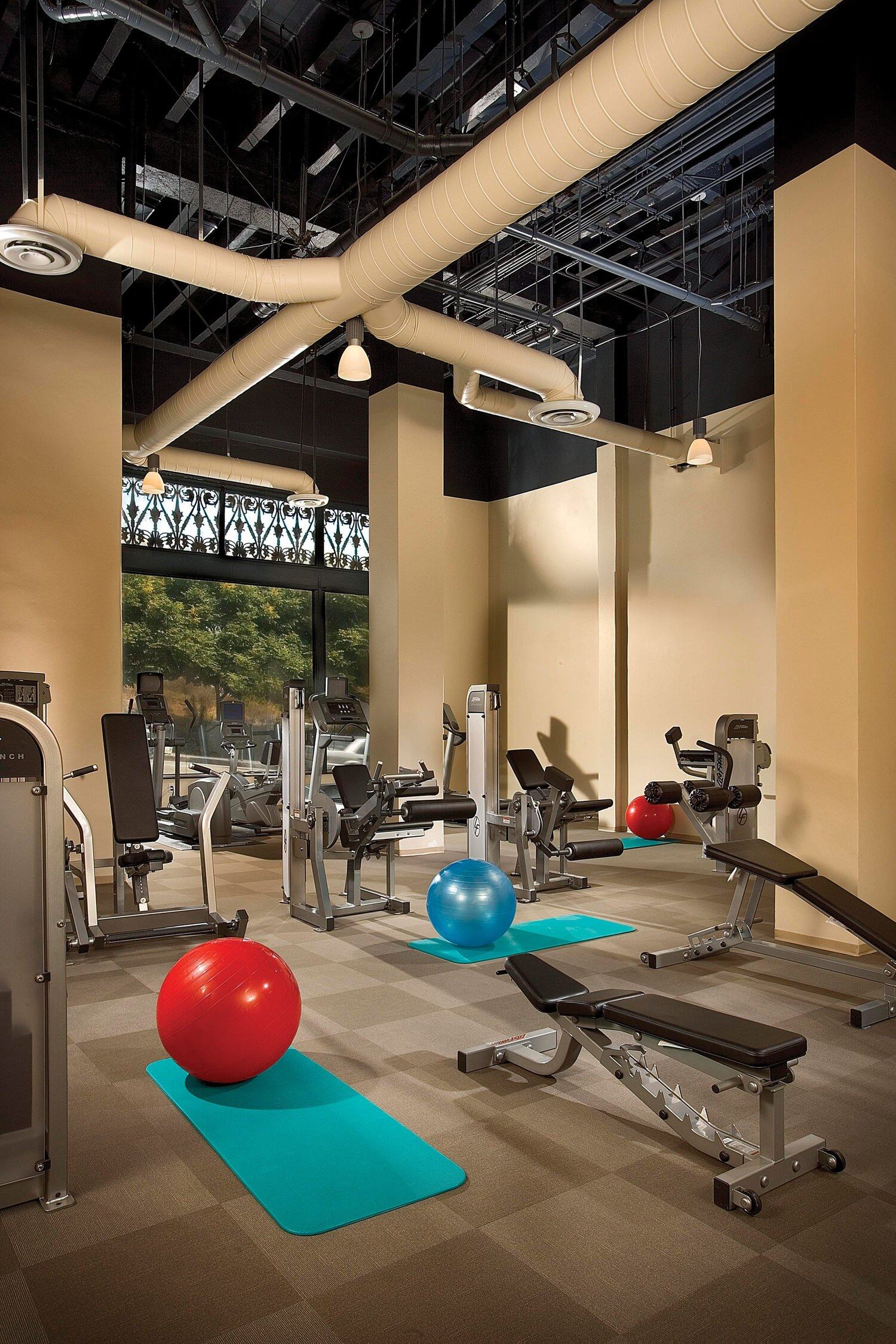 A gym that is full of exercise machines and equipment along the area of the room.
