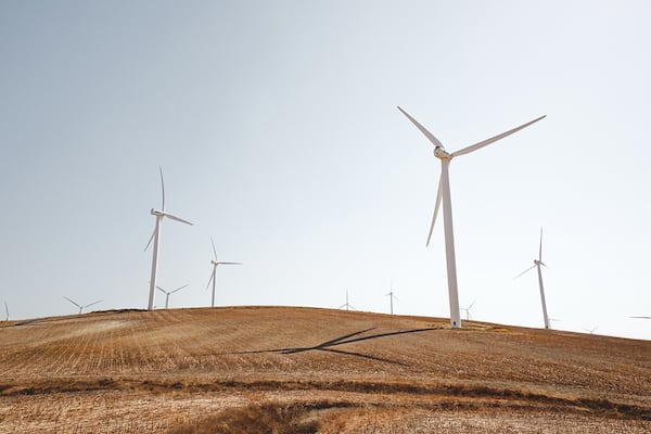 Several wind turbines are in motion on top of a small hill. The windmills are facing the same direction.