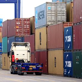 Semi truck driving in front of stacks logistics containers