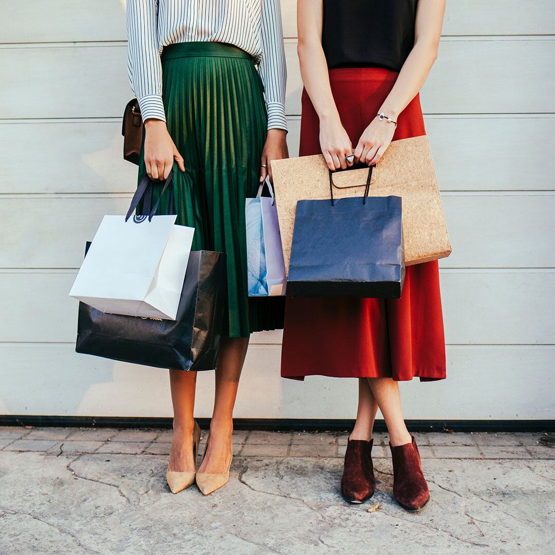 Two elegant unrecognisable women holding paper shopping  bags and standing in front of garage doors.