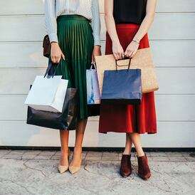 Two elegant unrecognisable women holding paper shopping  bags and standing in front of garage doors.